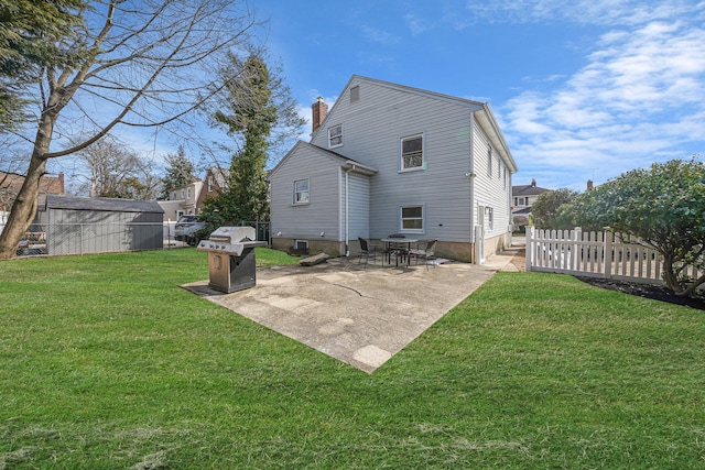 rear view of house with a lawn, a patio, a chimney, an outbuilding, and fence