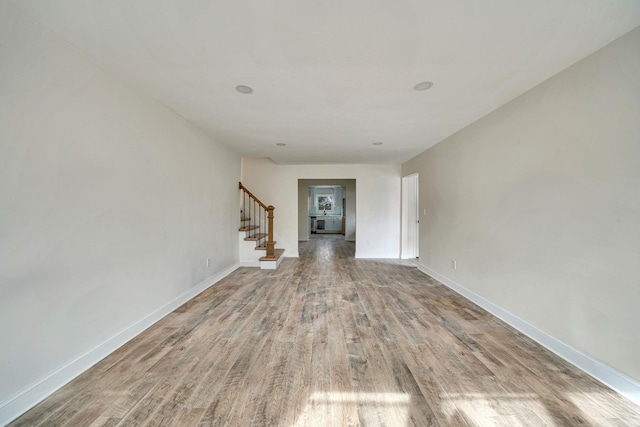 spare room featuring baseboards, stairway, and wood finished floors