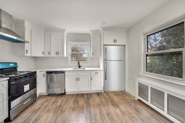 kitchen with a sink, light countertops, appliances with stainless steel finishes, wall chimney range hood, and radiator heating unit