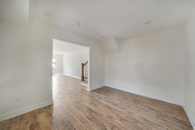 empty room with stairs, wood finished floors, and baseboards