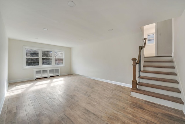 unfurnished living room with radiator, stairway, wood finished floors, and baseboards