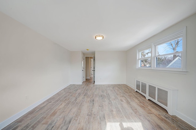 unfurnished room featuring light wood-type flooring, baseboards, and radiator heating unit