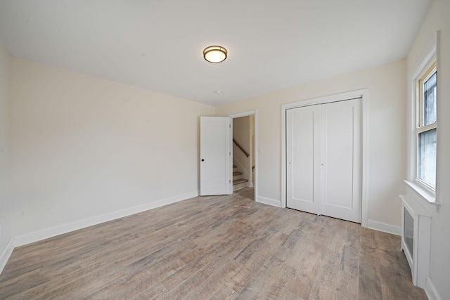 unfurnished bedroom featuring a closet, multiple windows, baseboards, and wood finished floors