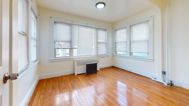 spare room with baseboards, light wood-type flooring, and radiator