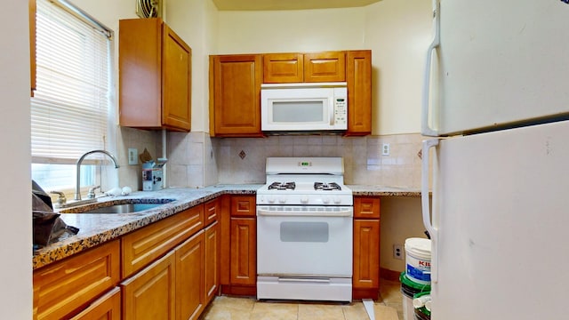 kitchen featuring brown cabinets, tasteful backsplash, a sink, light stone countertops, and white appliances