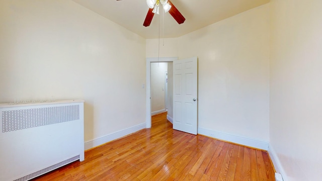 empty room featuring radiator, ceiling fan, light wood finished floors, and baseboards