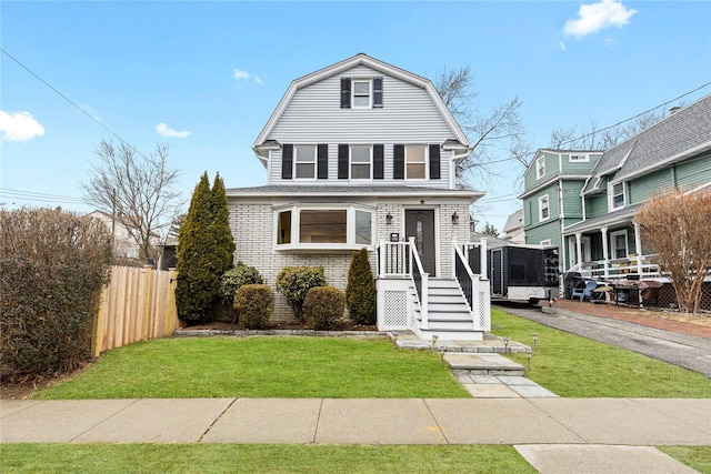 colonial inspired home featuring a gambrel roof, a front lawn, aphalt driveway, fence, and brick siding