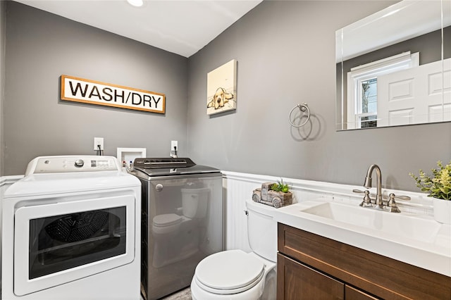 laundry room featuring a sink, a wainscoted wall, washing machine and dryer, and laundry area