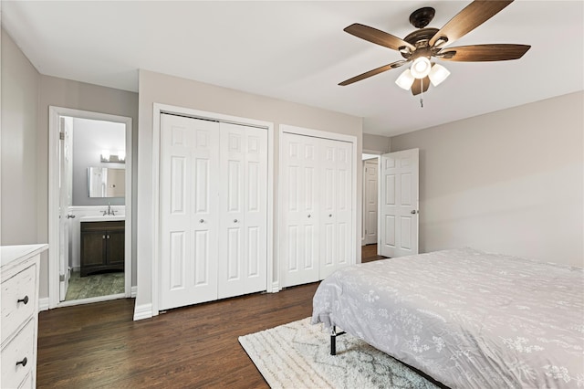 bedroom with two closets, baseboards, dark wood-style flooring, ensuite bathroom, and a sink