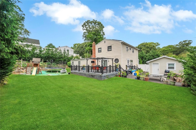 back of property with a pergola, an outbuilding, a trampoline, a wooden deck, and a playground