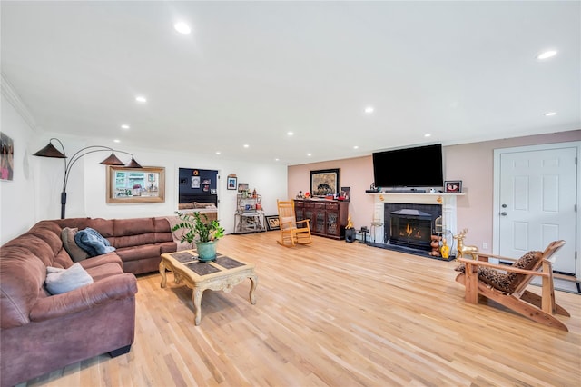 living area with light wood-style flooring, ornamental molding, a glass covered fireplace, and recessed lighting