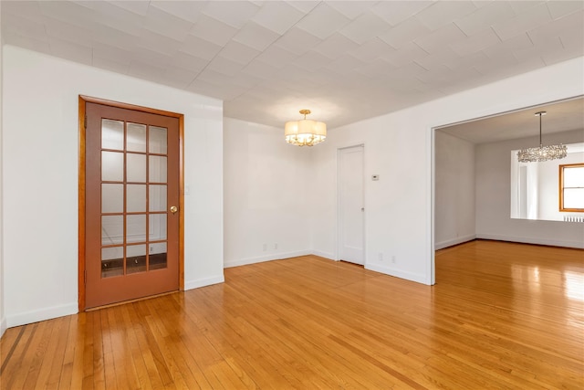 unfurnished room featuring a chandelier, light wood-style floors, and baseboards