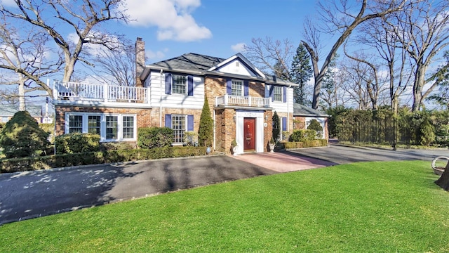 georgian-style home featuring aphalt driveway, brick siding, a chimney, a front yard, and a balcony