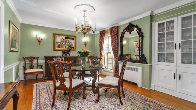 dining space with ornamental molding, radiator heating unit, wood finished floors, and an inviting chandelier