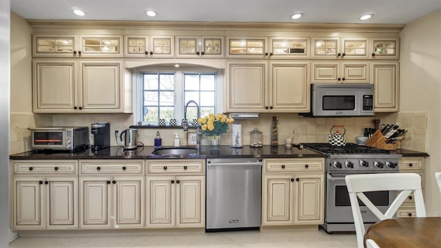 kitchen featuring a toaster, backsplash, stainless steel appliances, cream cabinetry, and a sink