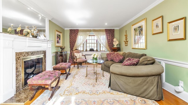 living room with a wainscoted wall, crown molding, wood finished floors, and a high end fireplace