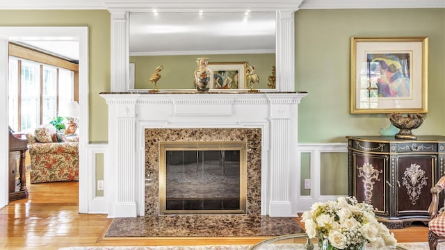 living room featuring wainscoting, ornamental molding, wood finished floors, a decorative wall, and a high end fireplace