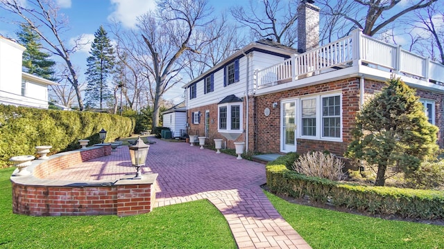 view of property exterior featuring a chimney, brick siding, a lawn, and a balcony