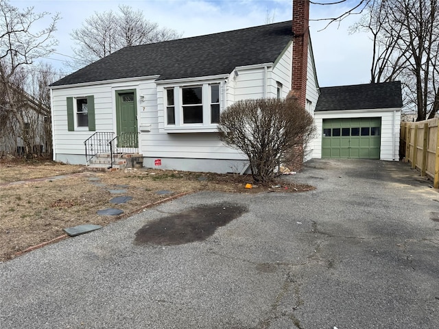 view of front of house featuring an attached garage, driveway, a chimney, and roof with shingles