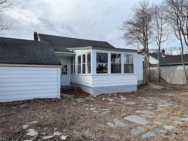 back of house with a sunroom, a chimney, fence, and roof with shingles