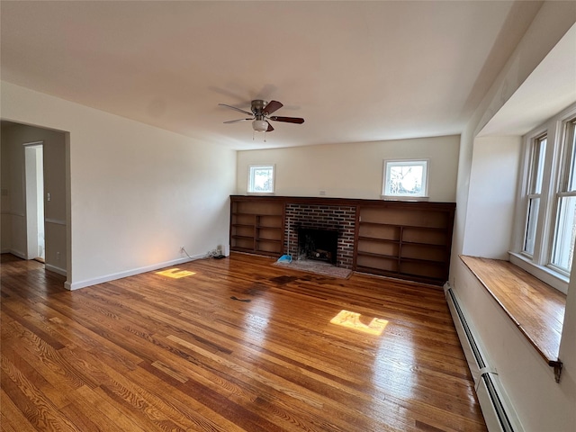 unfurnished living room with a baseboard heating unit, a healthy amount of sunlight, a fireplace, and wood finished floors