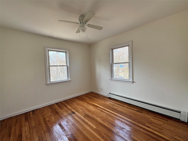 empty room featuring a baseboard heating unit, wood finished floors, a ceiling fan, and baseboards