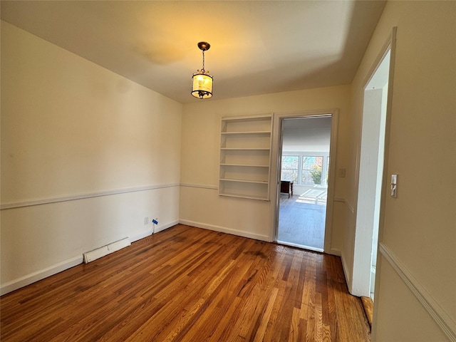 unfurnished dining area featuring a baseboard heating unit, built in shelves, wood finished floors, and baseboards