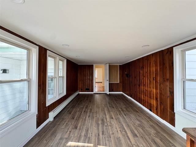 spare room featuring a baseboard radiator, wood walls, baseboards, and wood finished floors