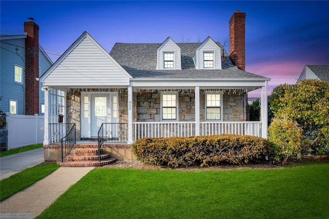 cape cod-style house featuring a porch, fence, stone siding, a chimney, and a front yard