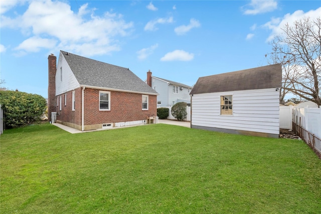 rear view of house with a lawn, a fenced backyard, a chimney, an outdoor structure, and brick siding