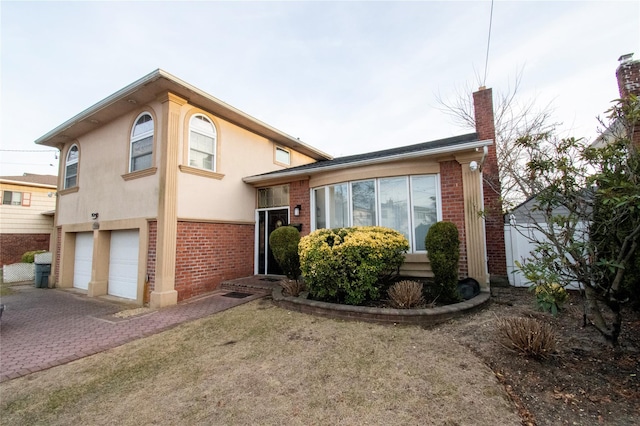 tri-level home with an attached garage, brick siding, decorative driveway, stucco siding, and a chimney