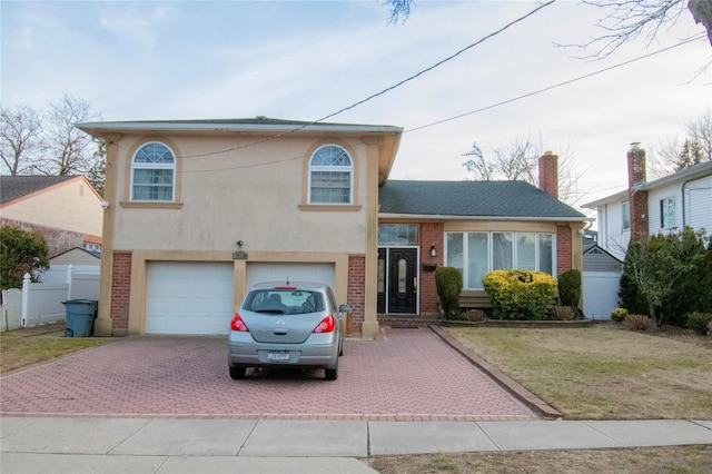 tri-level home featuring a garage, brick siding, fence, decorative driveway, and stucco siding