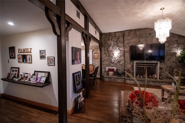 living area with visible vents, vaulted ceiling, a stone fireplace, wood finished floors, and baseboards