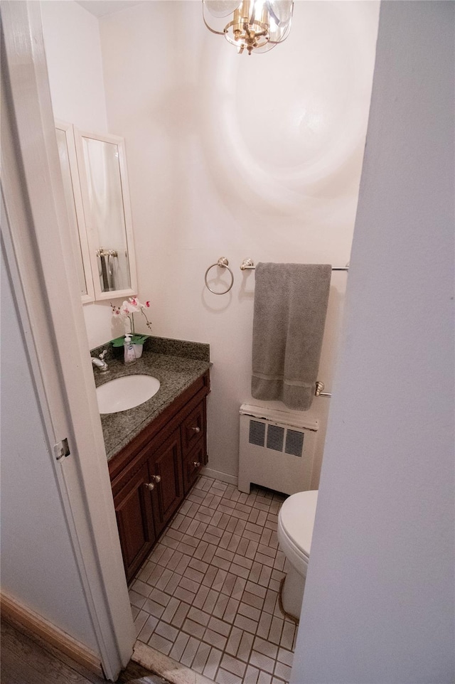 half bath with radiator, an inviting chandelier, toilet, and vanity