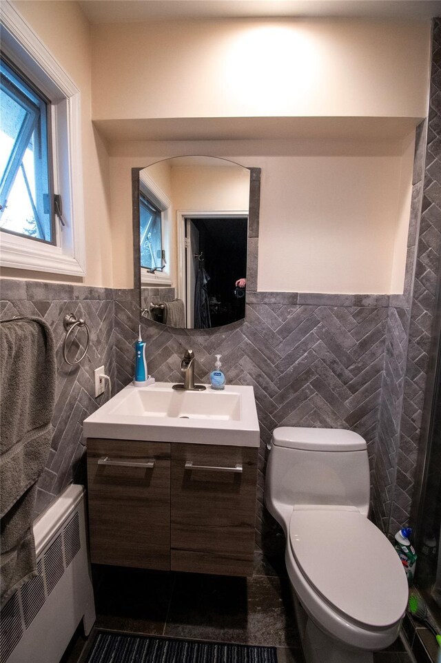 bathroom featuring tile walls, toilet, radiator heating unit, wainscoting, and vanity