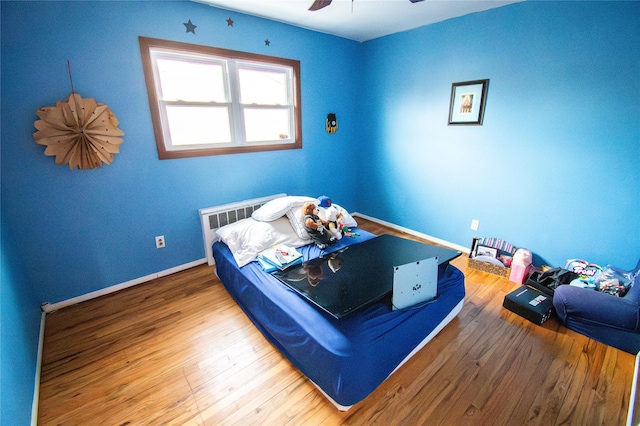 bedroom with radiator heating unit, wood finished floors, a ceiling fan, and baseboards