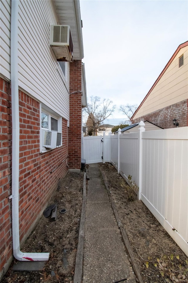 view of side of home featuring cooling unit, a gate, brick siding, and fence