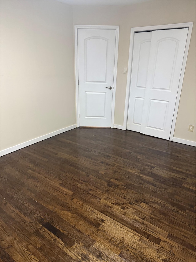 unfurnished bedroom with a closet, dark wood-style flooring, and baseboards