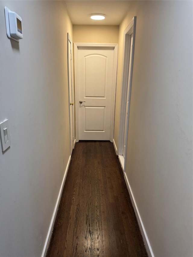 corridor featuring dark wood-type flooring and baseboards