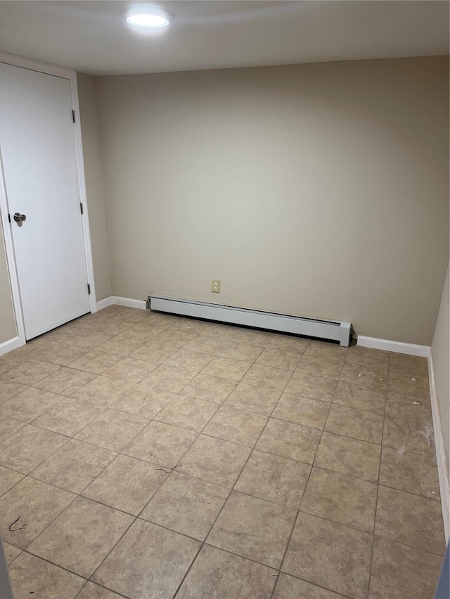 spare room with a baseboard heating unit, light tile patterned flooring, and baseboards