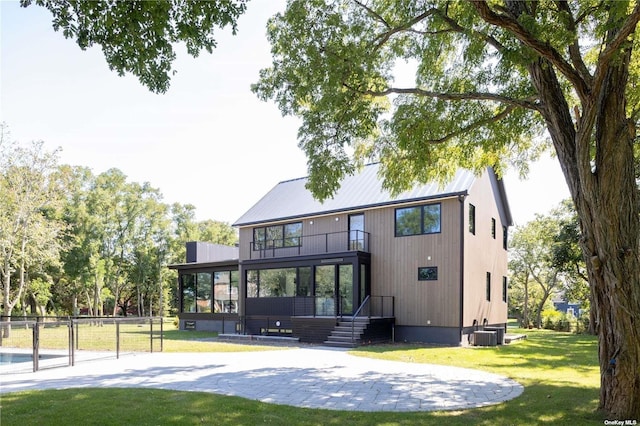 back of house with a balcony, central AC, fence, and a lawn