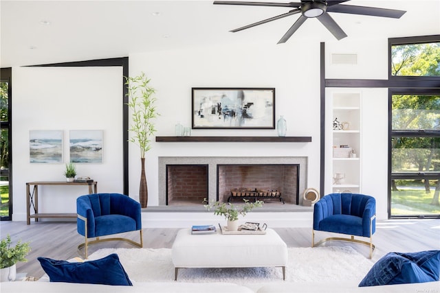 living area featuring a fireplace with raised hearth, built in shelves, wood finished floors, and visible vents