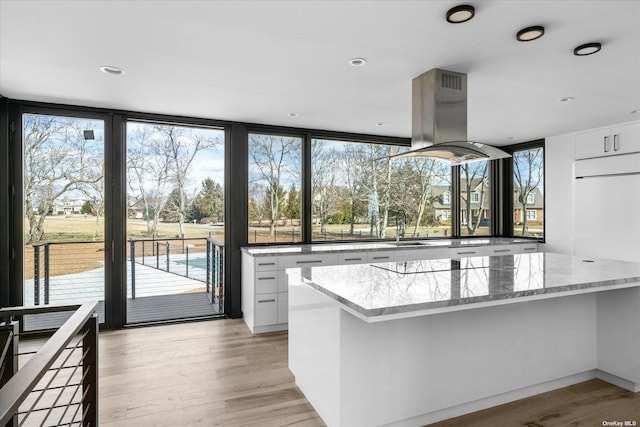 kitchen with light stone counters, white cabinetry, island range hood, modern cabinets, and light wood-type flooring