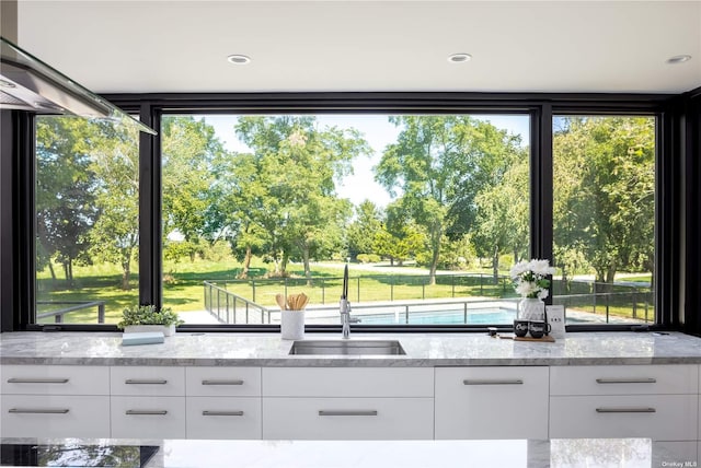 kitchen with modern cabinets, light stone countertops, black electric cooktop, white cabinetry, and a sink