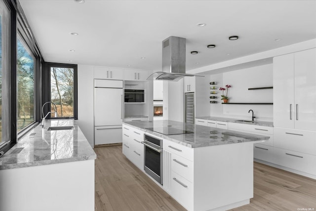 kitchen featuring a center island, paneled built in fridge, a sink, stainless steel oven, and island range hood