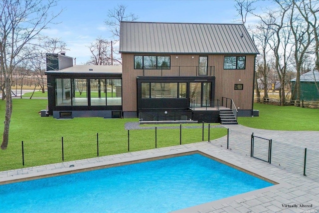 rear view of house with a patio, a sunroom, a lawn, an outdoor pool, and a chimney