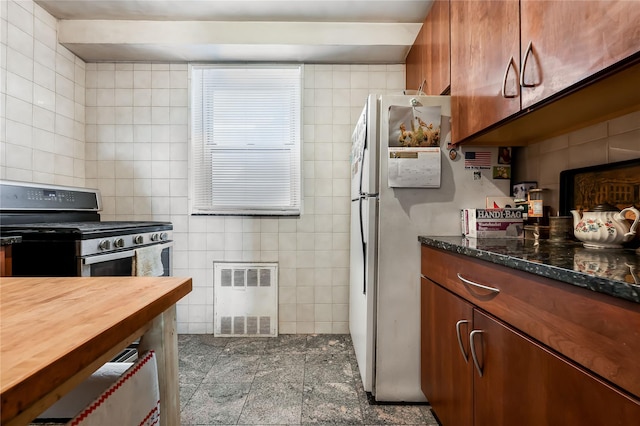 kitchen with brown cabinets, tile walls, wooden counters, freestanding refrigerator, and gas range