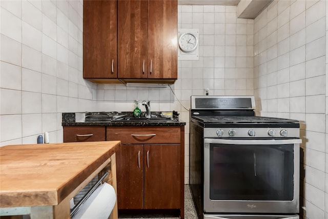 kitchen featuring stainless steel gas stove, a sink, tile walls, and brown cabinets