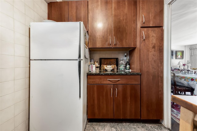 kitchen featuring tile walls, freestanding refrigerator, decorative backsplash, dark stone counters, and brown cabinetry