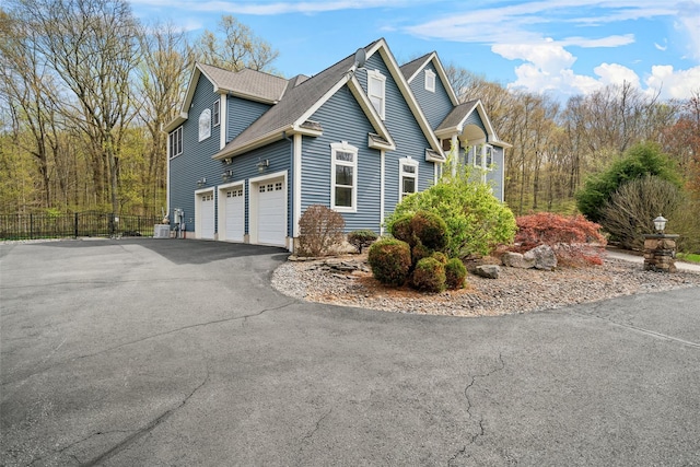 view of property exterior featuring fence, a shingled roof, an attached garage, and driveway